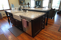 Thumb kitchen  rustic style  black painted island with sand through  apron sink  raised bar with turned posts legs  plant on door on end of the island