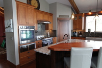 Thumb kitchen  shaker style  cherry  medium color  recessed panel  accent color island  raised neck with wood top  craftsman glass grid door panels at the top  two drawers below ovens